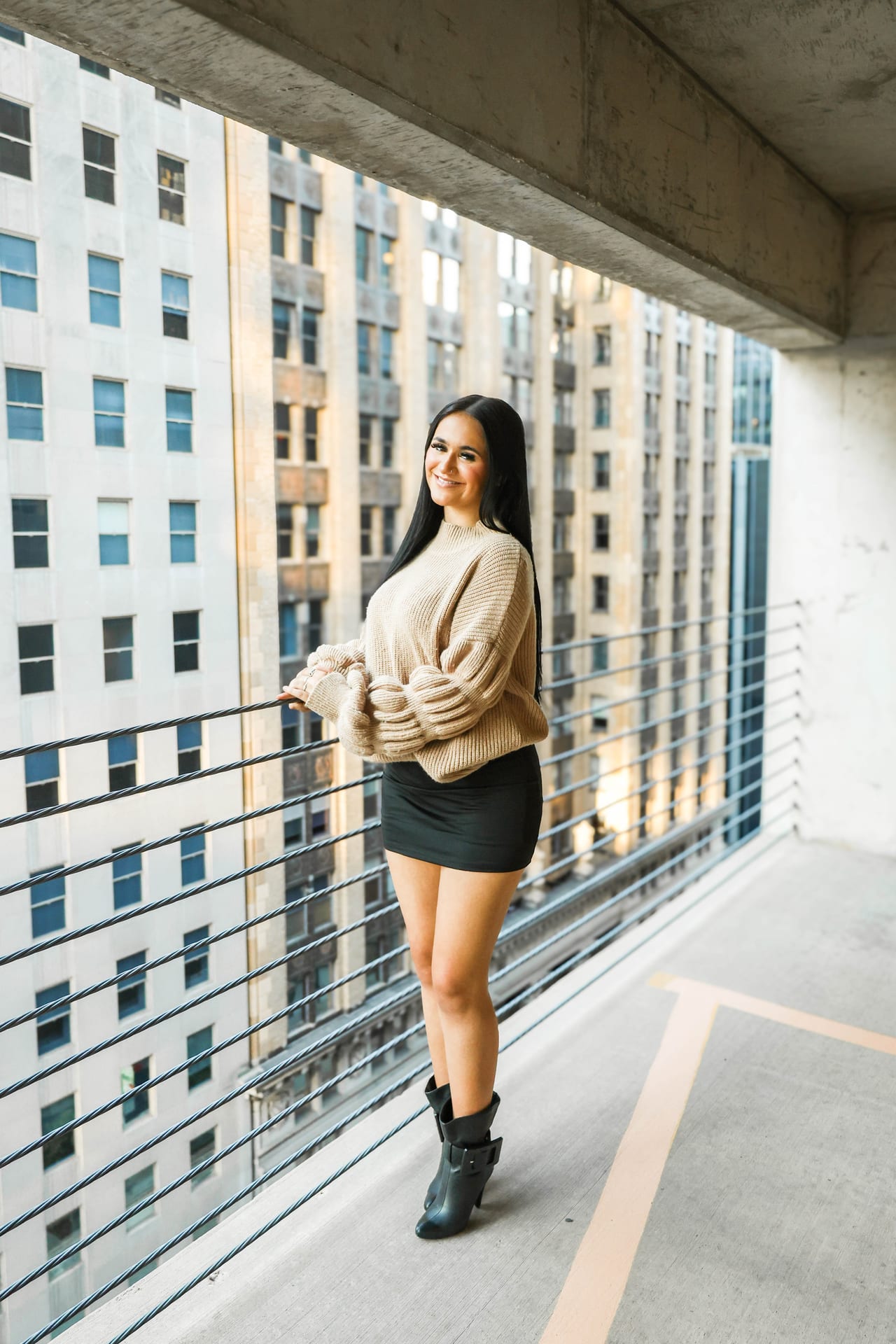 Senior in tan sweater on an urban high-rise balcony