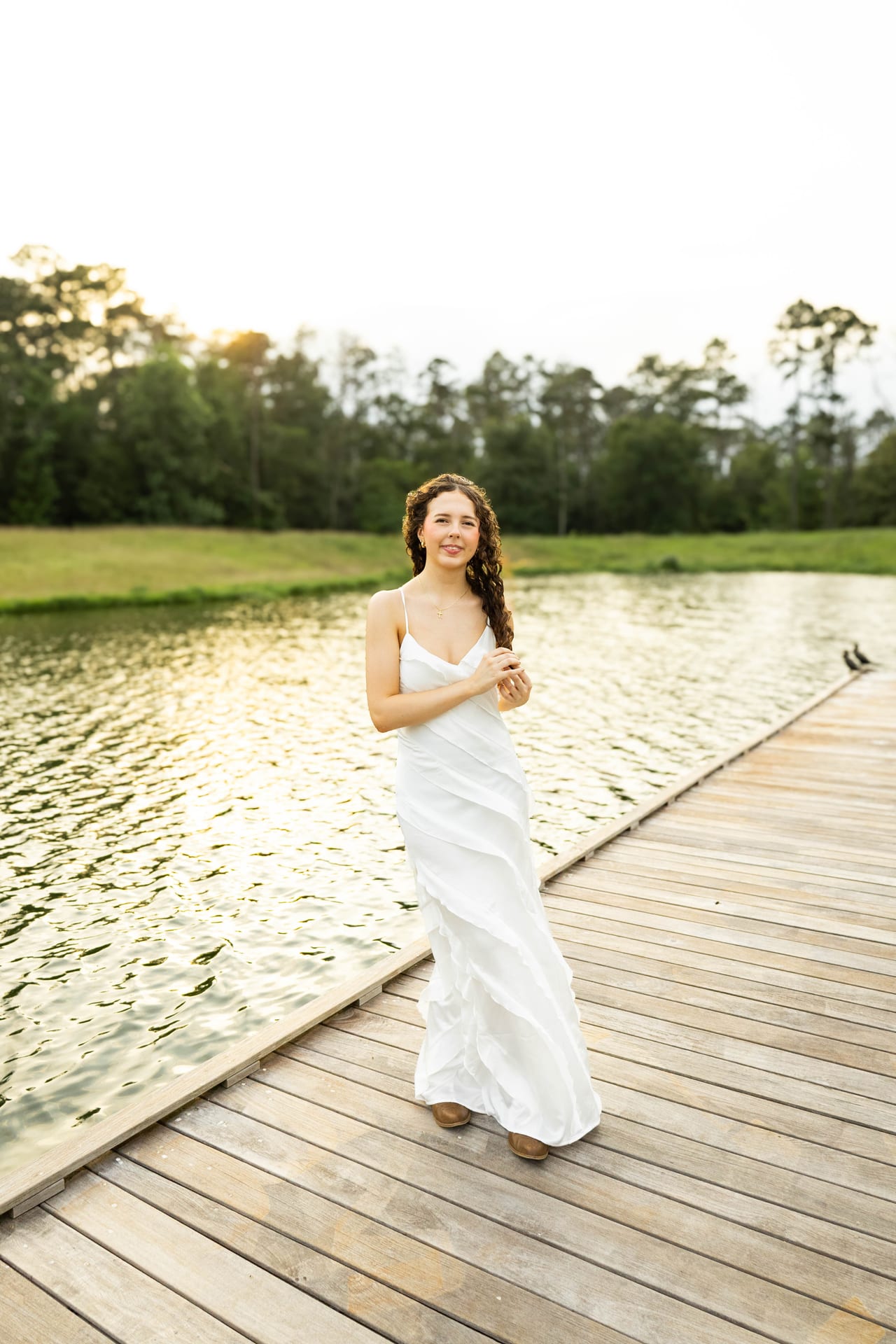Senior in white slip dress on a wooden dock by the lake
