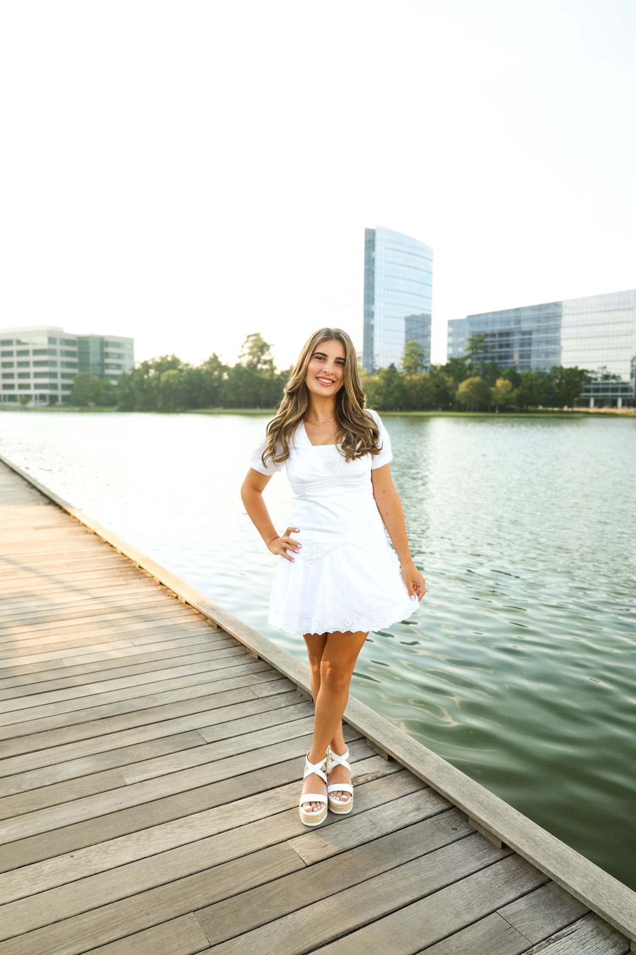 Senior in white dress on a wooden dock with downtown Houston behind