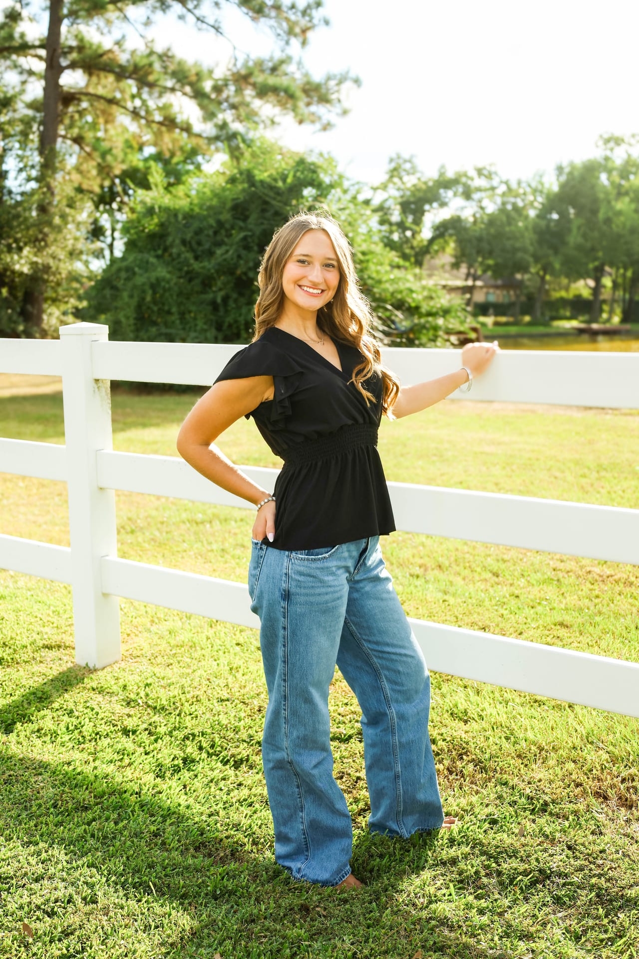 Senior in black peplum top and jeans by a white fence