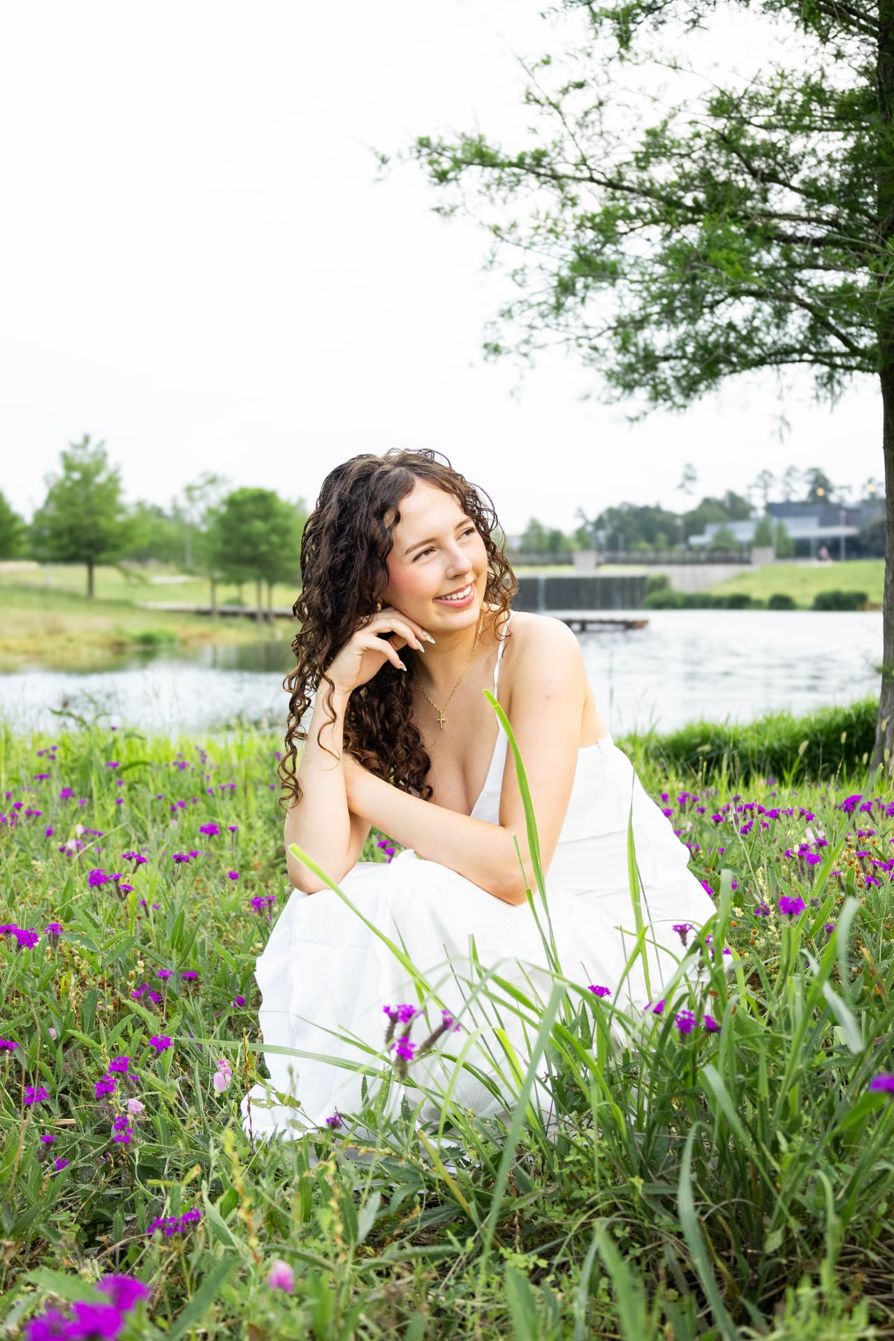 Senior in white dress sitting in a field of purple wildflowers