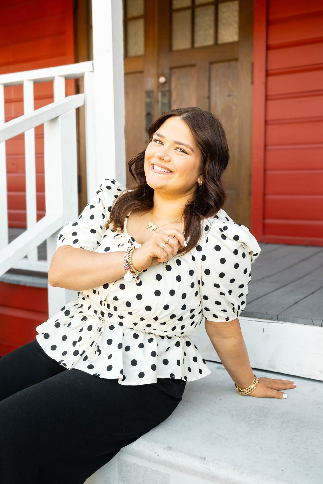 Senior in white polka-dot top sitting on porch steps by a red door
