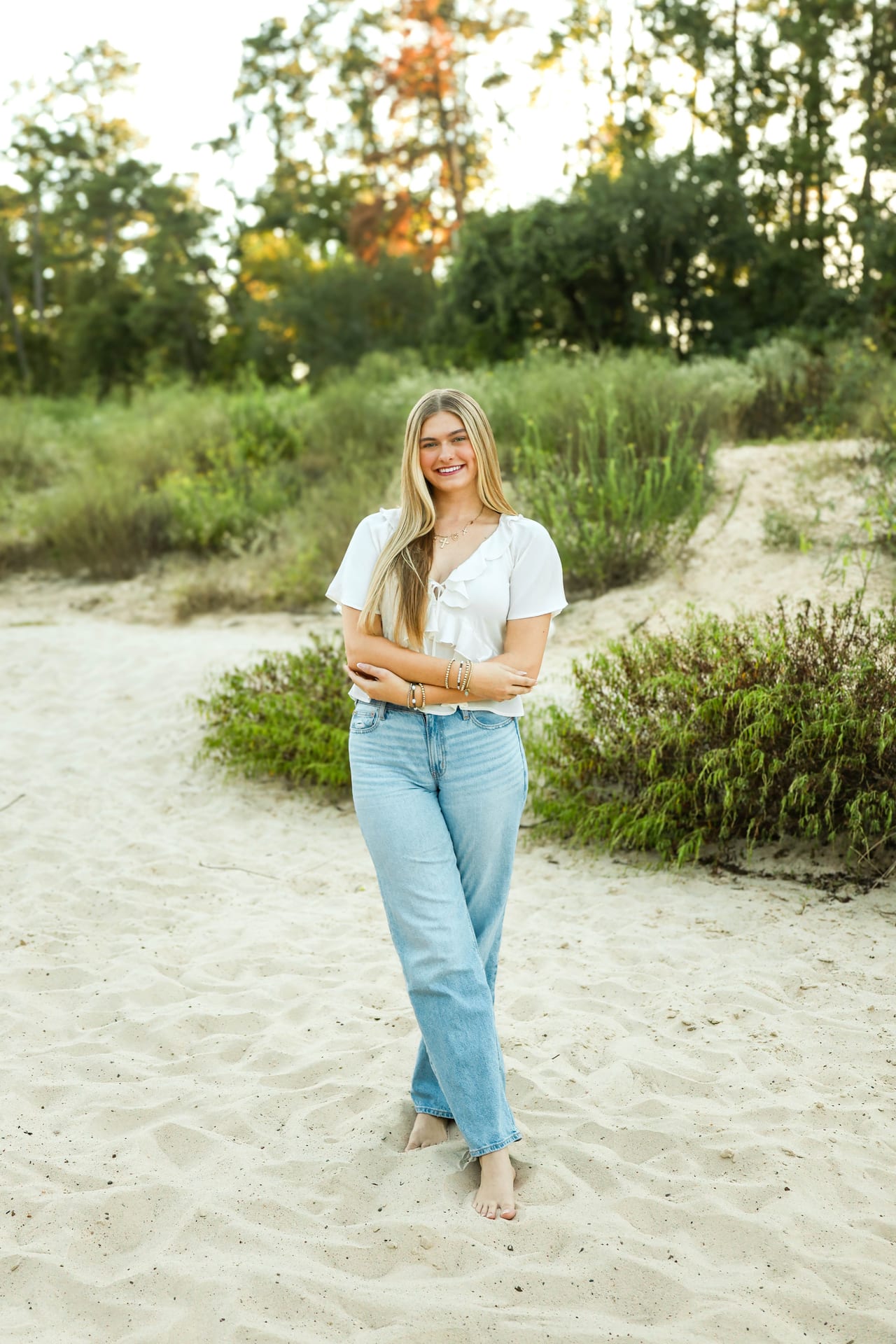 Senior in white top and jeans barefoot on a sandy path at golden hour