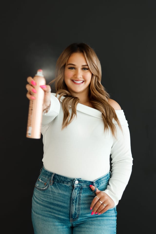 Stylist holding hairspray against a dark studio backdrop